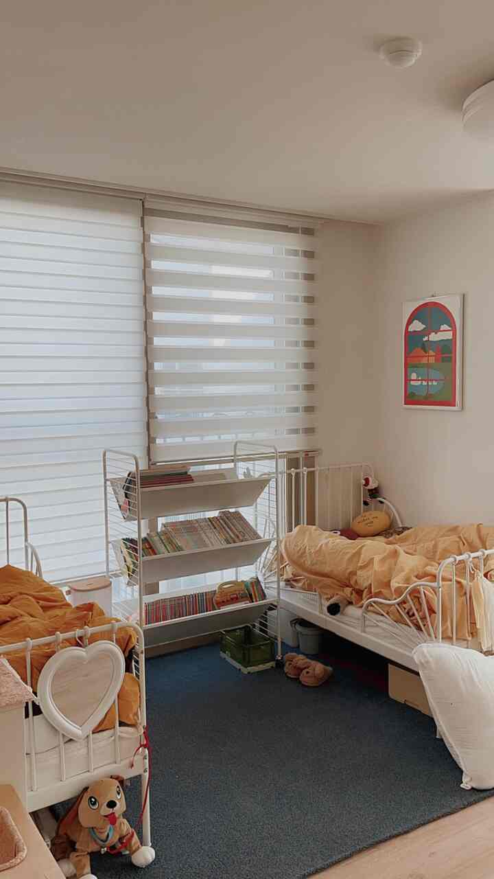 A white and orange toned kids' room featuring two beds and a book rack trolley creating a cozy atmosphere