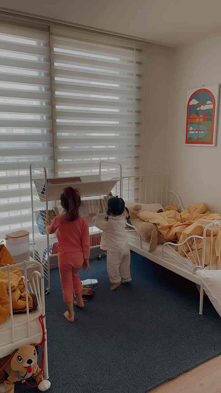 A white and yellow toned kids' room featuring a book trolley and two children, creating a cozy and bright atmosphere