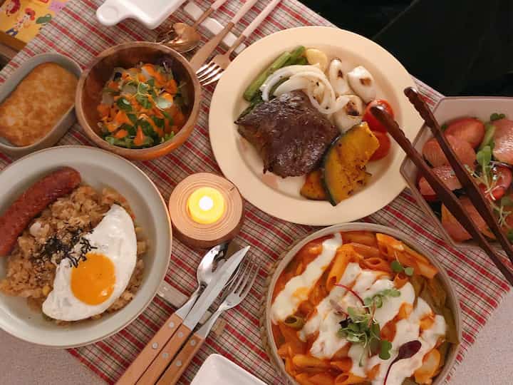 A modern dining setting featuring a red plaid tablecloth with various plates, wooden cups, and a candle