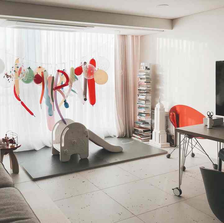 白とライトグレーの色調のリビング兼子供部屋、中央に子供用滑り台と風船デコレーションが配された明るく居心地の良いインテリア