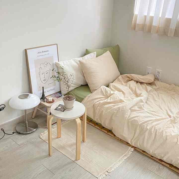 ベージュ色調の寝室、緑のクッション付きベッド、木製スツールとポスターが印象的な雰囲気を演出