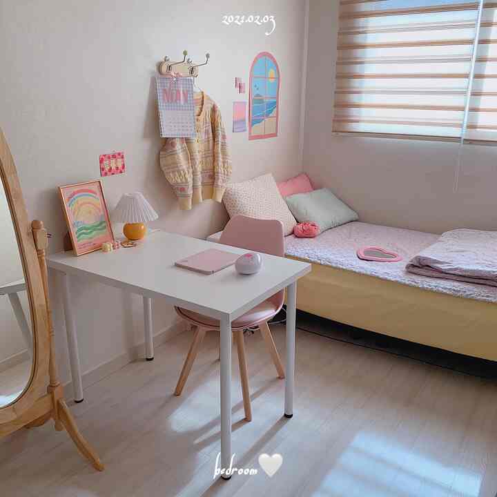 柔らかなピンクとホワイトのトーンのワンルーム寝室、机とピンクの椅子、全身鏡が配置された居心地の良い空間