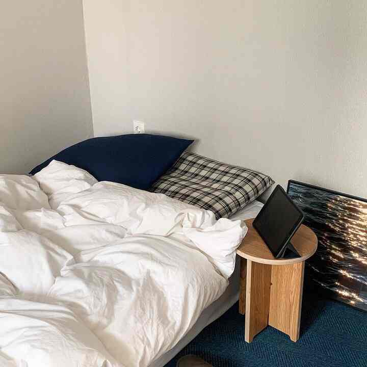 A cozy bedroom in white and navy tones featuring minimal wood stool and rug, presenting a clean and simple design