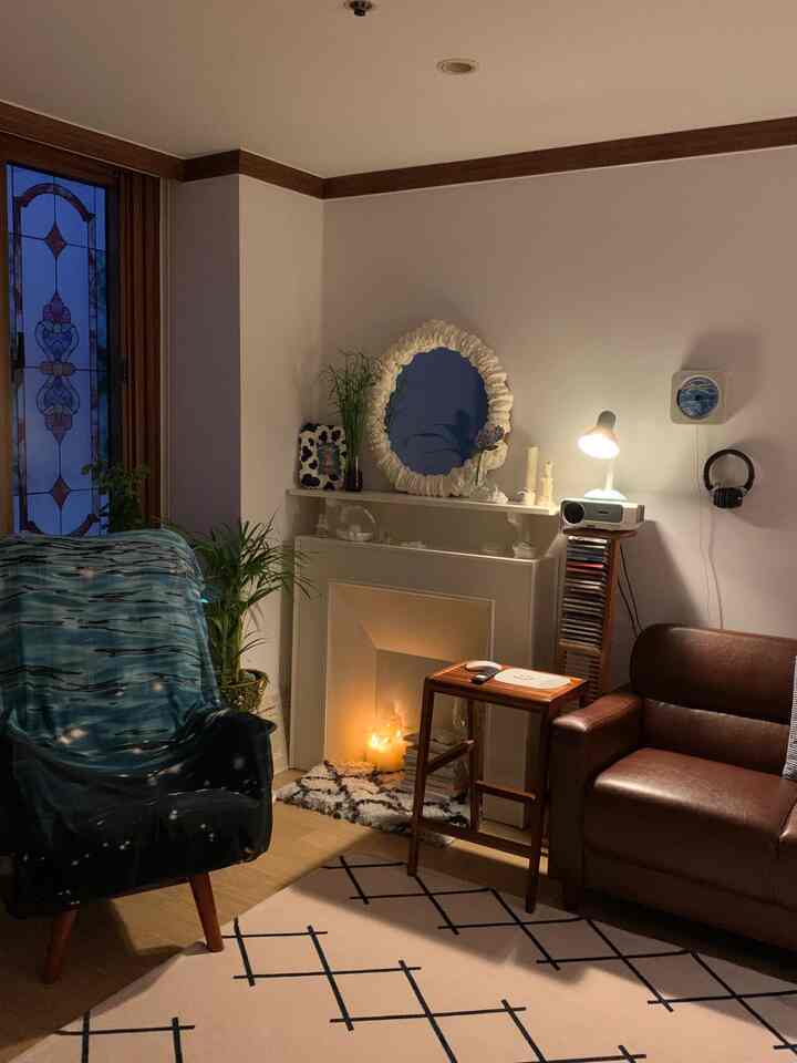 A cozy living room in brown and white tones featuring a fireplace, distinctive mirror, sofa, and stool