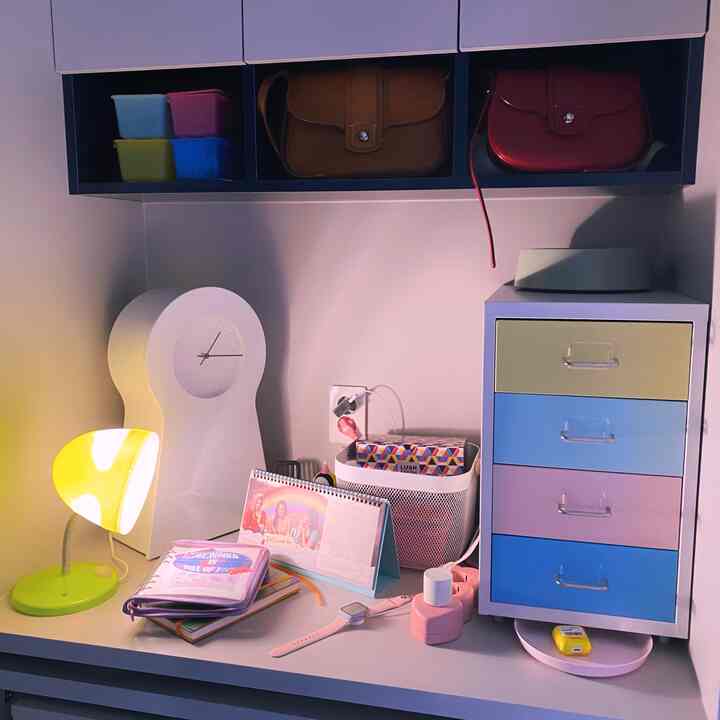 パステルトーンのデスクスペース、カラフルな引き出しとIKEAの時計、照明付きのデスクランプが配置された雰囲気のあるハイティーンスタイルのインテリア