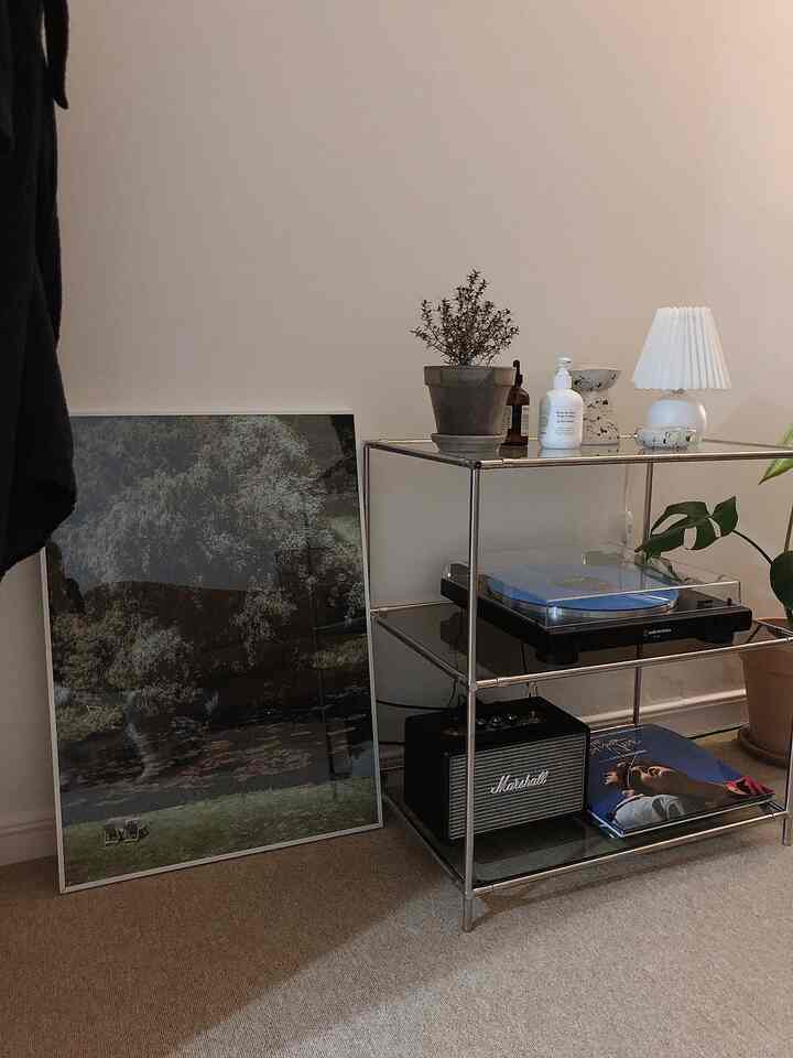 Natural wood tones and modern metal shelving in a living room corner music area, featuring posters, turntable, and lighting in a simple setup