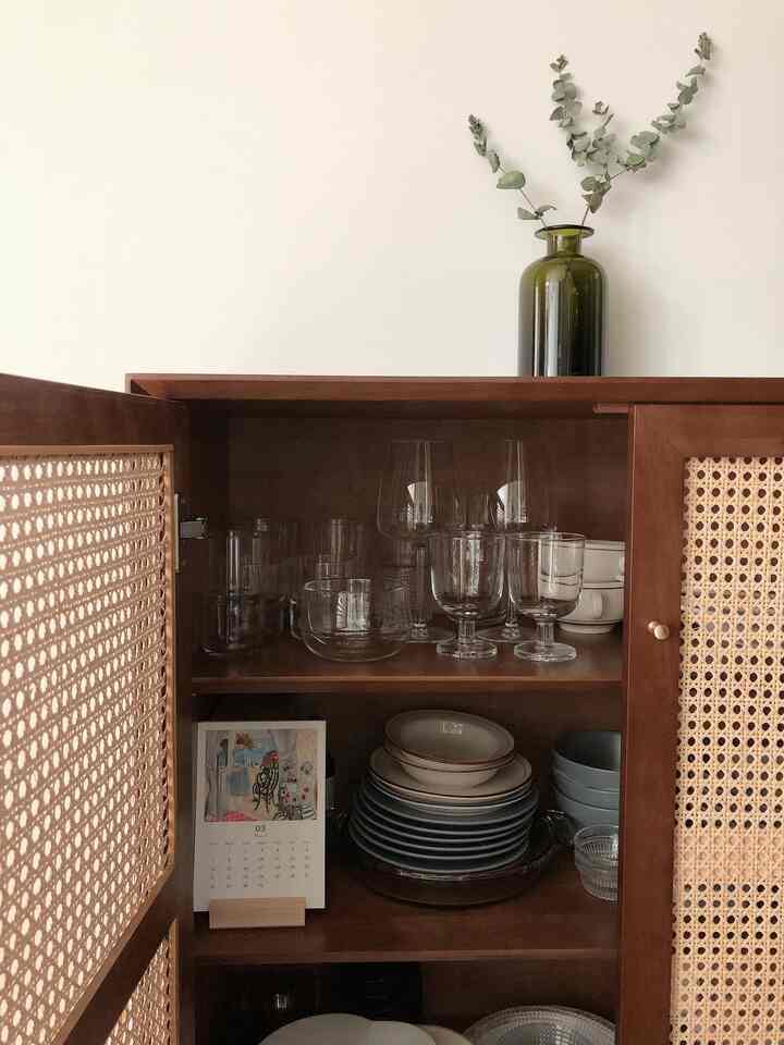 濃い木目調とラタンのディテールがある廊下用食器収納キャビネットが配置されたナチュラルな玄関空間