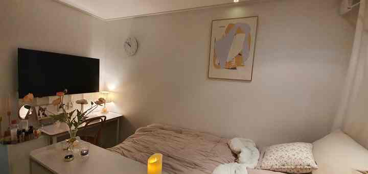 Beige-toned small bedroom featuring a bed, desk, and table lamp creating a cozy atmosphere