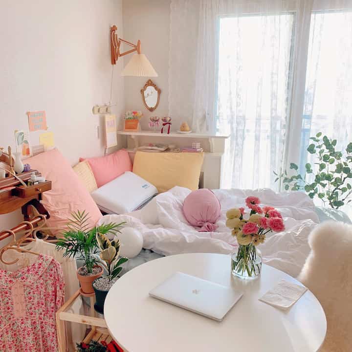 Bright white and pink bedroom featuring cozy pillows and indoor plants with soft natural light