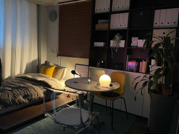 White and wood tone bedroom featuring wooden blinds, round table with warm lighting in a cozy cafe-style interior