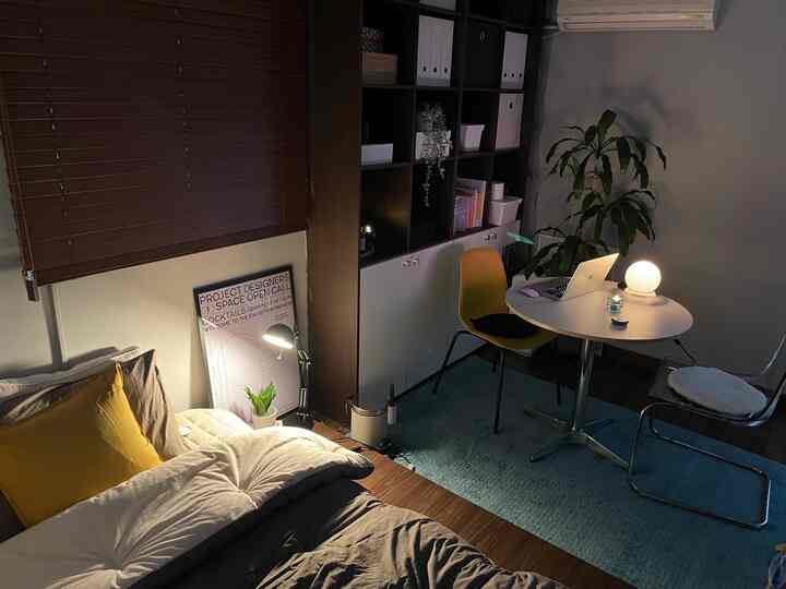 Natural modern bedroom with brown floor and yellow chair, featuring a round table lit by lamps with a laptop on top, creating a cozy atmosphere