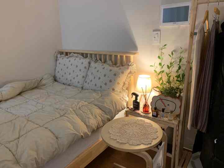 ナチュラルなベージュトーンの寝室、木製のベッドと花柄の枕、雰囲気のあるムードランプが配置された落ち着いた空間