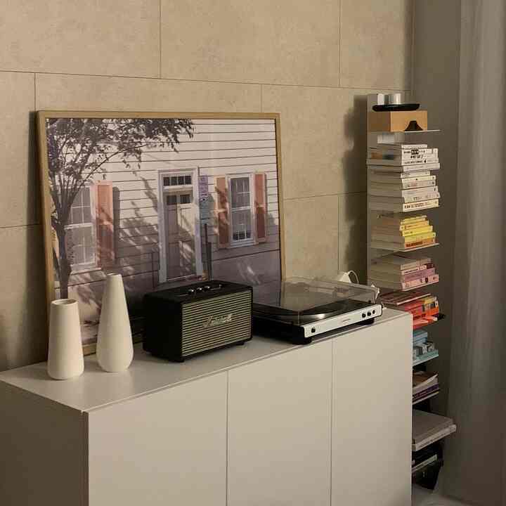 White-toned living room space featuring white cabinet with vases, Bluetooth speaker, turntable, and framed art in a modern interior