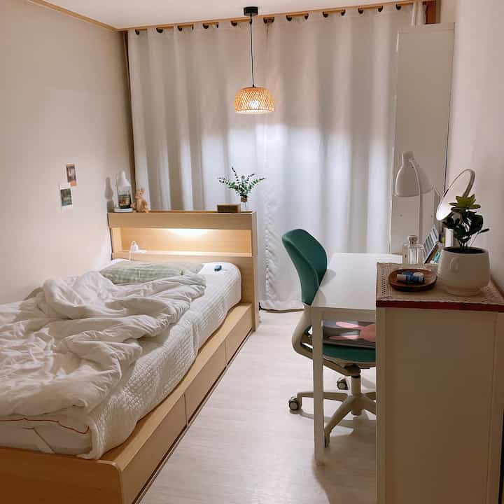 ホワイトと木目調の色合いが調和する一人暮らしの寝室、ベッドとデスク、ペンダントライトが配置された落ち着いた雰囲気のインテリア