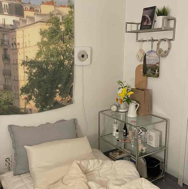 White and gray toned bedroom featuring a wall poster and stainless steel 3-tier shelf with decorative items in a natural, cozy setting