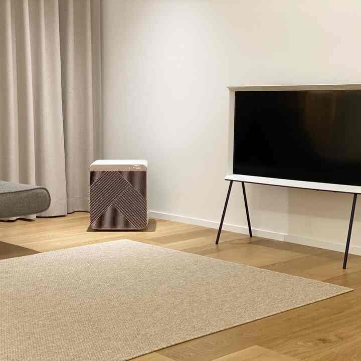 A clean living room with beige rug, wood-tone flooring, white walls, and a modern TV stand