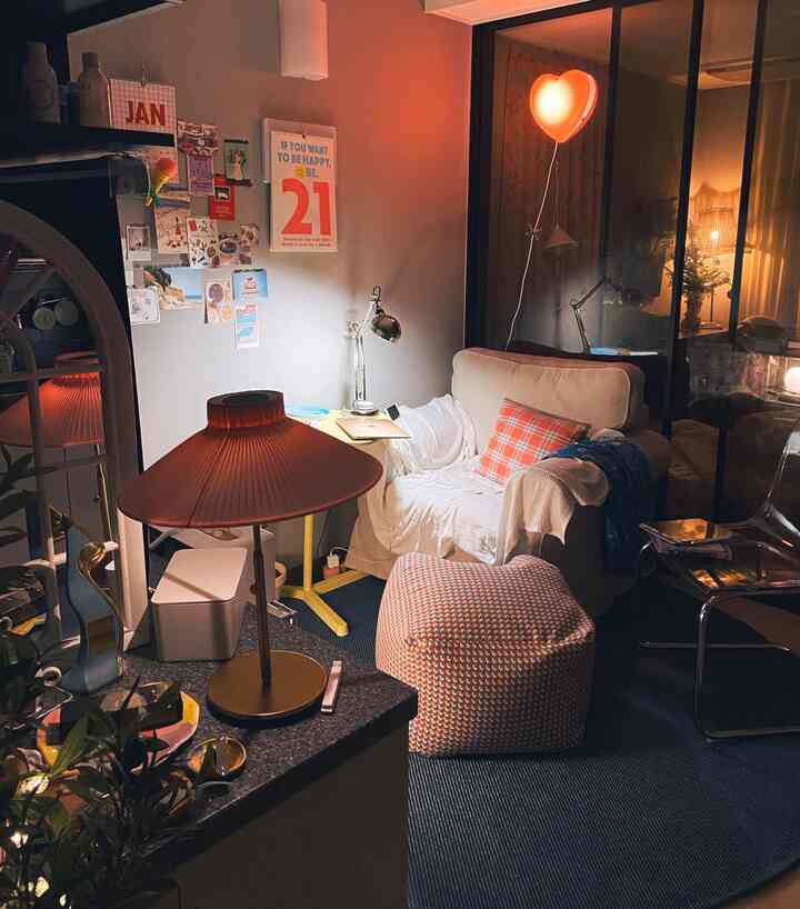 Warm orange and neutral toned living room featuring a white armchair, patterned stool, yellow side table, and pink heart-shaped wall lamp creating cozy atmosphere