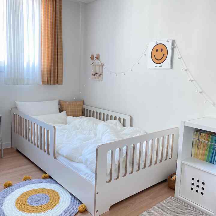 ホワイトとイエローの色調の子供部屋、木製ベッドとイエローチェックのカーテン、丸いラグが配置された温かみのあるインテリア