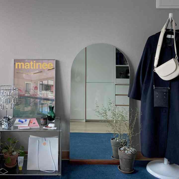 Soft natural tone living room featuring an arched mirror, potted plants, poster, and coat rack with a calm atmosphere