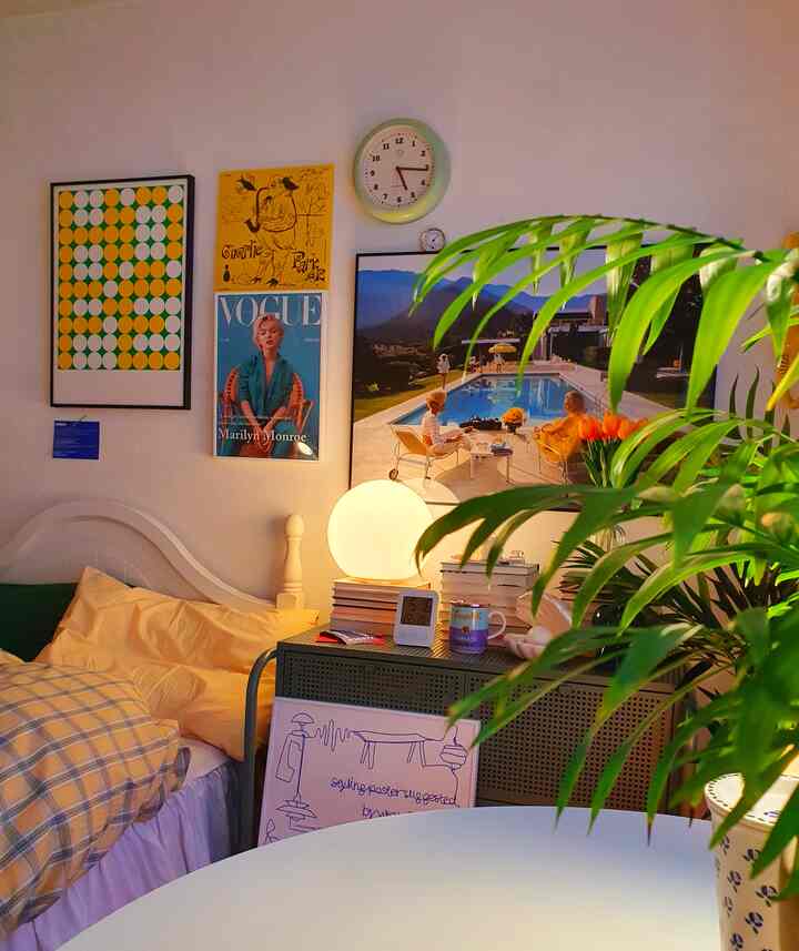 Modern bedroom with yellow bedding and lush green plants, posters and a clock decorate the wall creating a cozy atmosphere