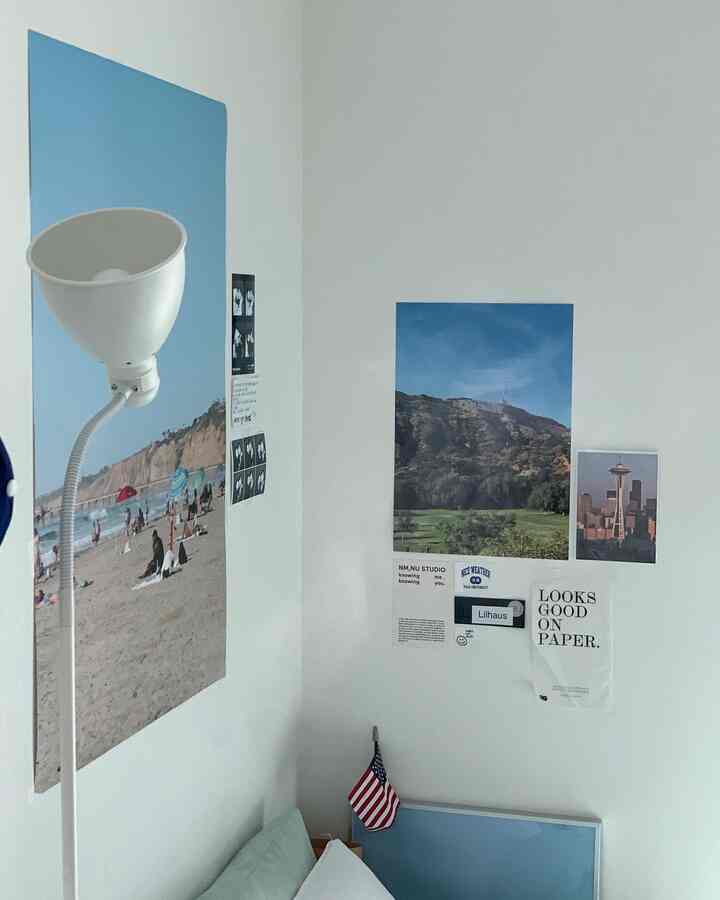 A bedroom corner with white walls and blue posters, featuring a floor lamp creating a simple and natural atmosphere