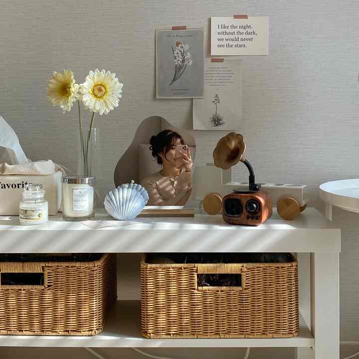 Natural toned and white side table featuring flowers, candles, vintage speaker, and curved mirror in a cozy interior space