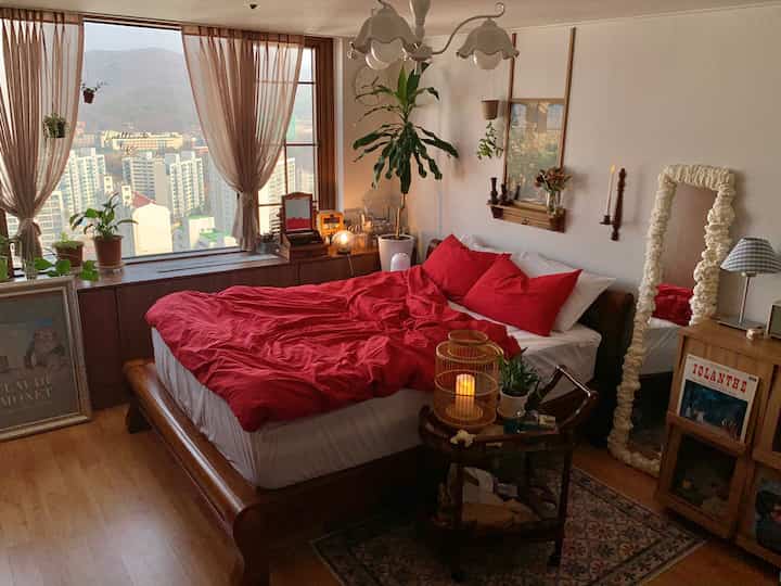 Cozy bedroom with red bedding and wood-tone furniture illuminated by natural light