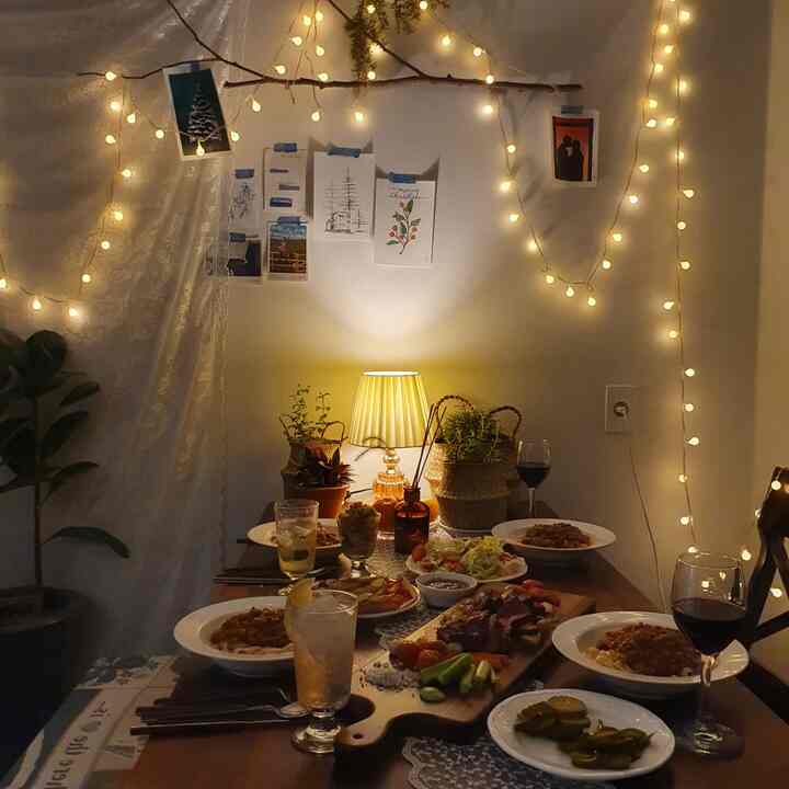 暖かいベージュとブラウンの色調のダイニング、ホームパーティの料理が並び、ストリングライトが雰囲気あるインテリア