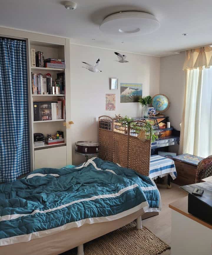 白と青のトーンの3坪の寝室兼ワークスペース、ラタンの間仕切りとビンテージ装飾が調和した居心地の良いコテージスタイルのインテリア