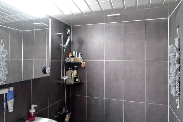 Modern bathroom with gray tiled walls, shower fixture, and corner shelves arranged neatly