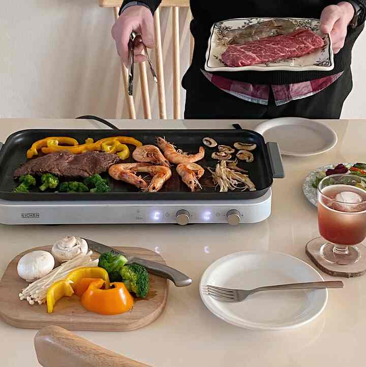 Yellow and wood tone kitchen table featuring a 2-burner induction with meat and vegetables grilling in a cozy home party setting