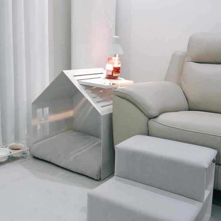 A modern living room in white and light gray tones featuring a dog house and pet steps neatly arranged beside a sofa