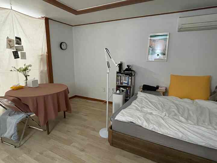 A white and brown toned single household bedroom featuring a bed, dining table, and curtain in a cozy setting