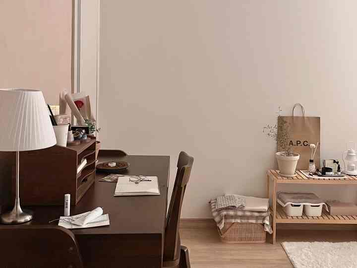 ナチュラルな木目調とベージュの壁のワンルーム、デスク、椅子、棚、植物が配置された雰囲気のあるホームオフィス空間