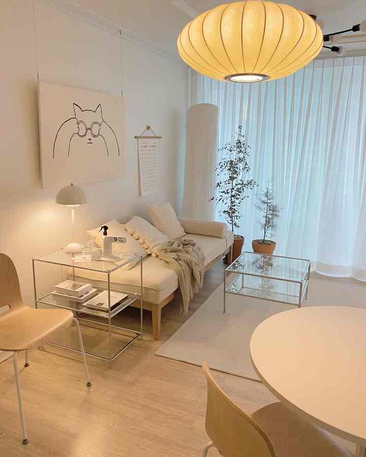 明るいホワイトと木目調が調和したモダンなリビング、ソファベッドとガラス棚、大きな丸い照明が配置された印象的な空間