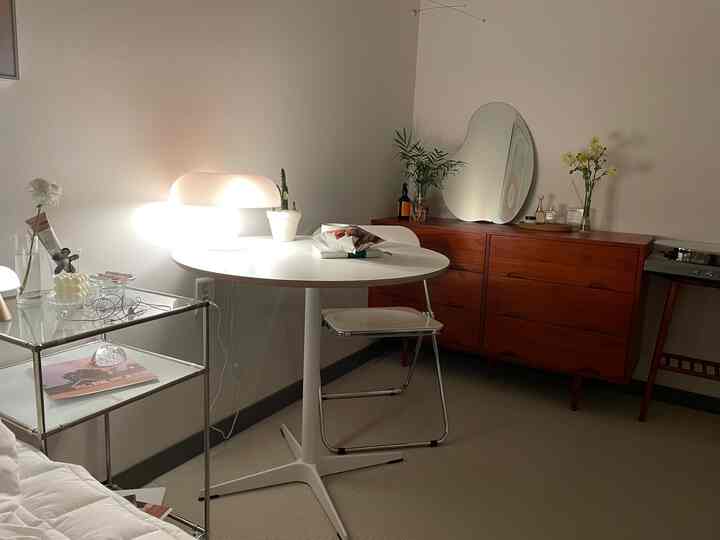 A white and brown toned living room featuring a round table, sideboard, and plants with a modern and natural atmosphere
