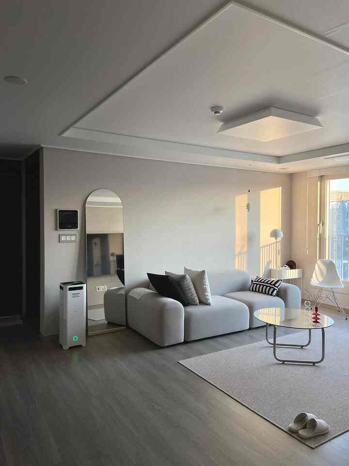 A white and gray toned living room featuring a gray sofa and glass coffee table in a simple modern space