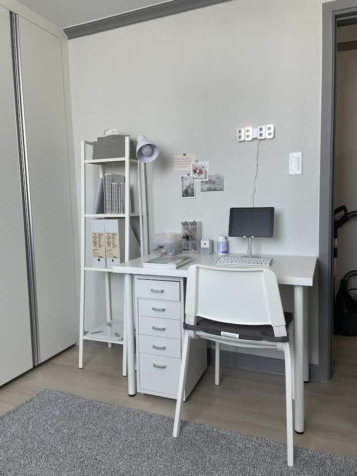 Compact home office space in white and gray tones featuring organized desk and bookshelf with simple modern interior