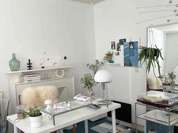 明るい白を基調としたワンルームのホームオフィス、モダンなデスクと全身鏡、複数の植物とテーブルランプが配置された清潔で現代的なインテリア
