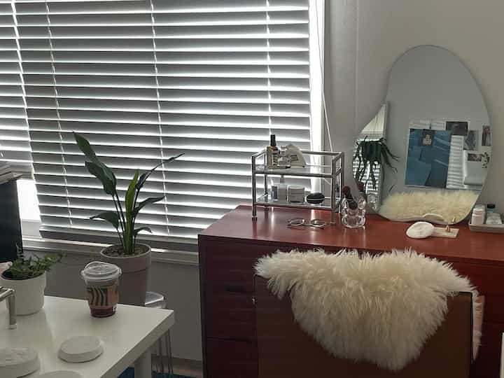 A simple interior featuring a white and wood tone vanity space with horizontal blinds covering the window and decorative plants