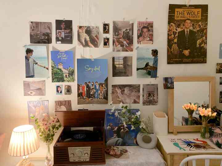 White wall adorned with various movie posters, featuring a wood-tone turntable and lamp in a retro-style bedroom space