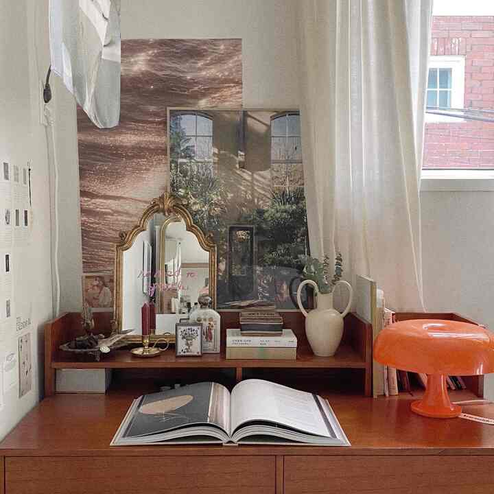 Natural-toned studio apartment featuring a vintage mirror, desk, and orange lighting with warm, cozy atmosphere