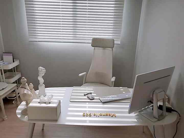 Bright white-toned simple modern home office featuring a white desk, ergonomic chair, and monitor in a clean workspace