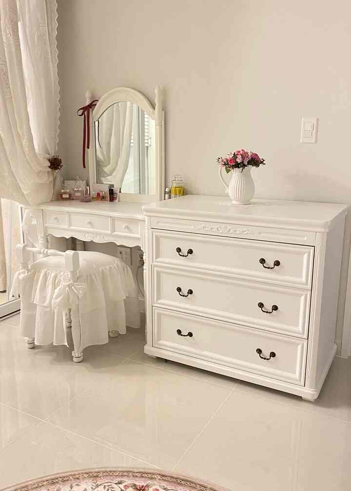 白を基調としたヴィンテージ風寝室、フリルの椅子と化粧台、花瓶が配置された雰囲気のあるインテリア