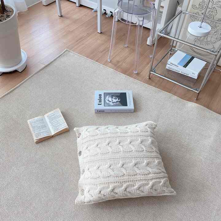 ベージュのラグとクリーム色のクッション、ウッドトーンの床が調和する居心地の良い北欧風の多目的空間