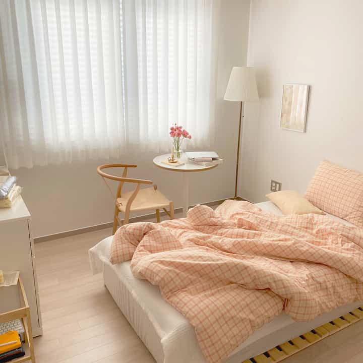Warm apricot and beige toned bedroom featuring plaid bedding and natural wood chair, creating cozy atmosphere