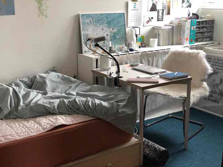 白い壁と青いラグが調和する一人用寝室、シンプルなデスクと椅子が配置された居心地の良いホームオフィス空間