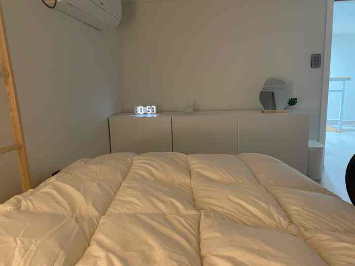 White-toned bedroom featuring a central white bed and minimal storage cabinet in a clean and simple space