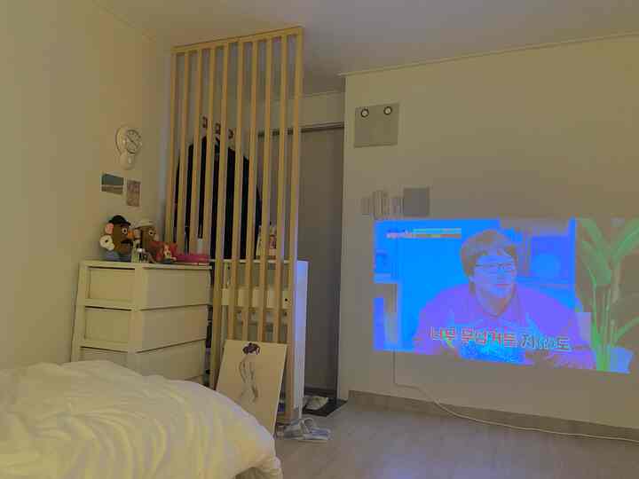 白と木目調の調和が取れたワンルーム寝室、ベッドと収納棚、壁にプロジェクター映像が投影された雰囲気のある空間