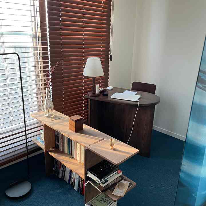 A compact study featuring wood tones and navy carpet, with a dark wood desk and bookshelf designed for remote work